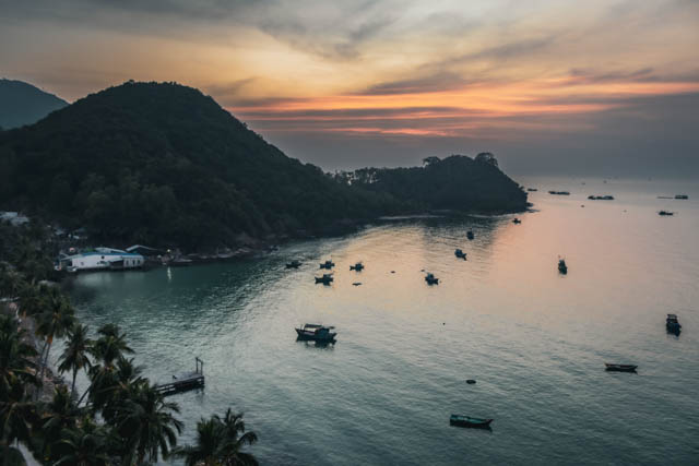 Tropical bay at dusk with boats and forested hills along the shore