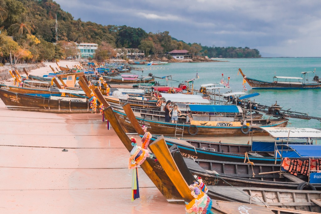 Long-tail boats on a sandy beach with turquoise water and green hills