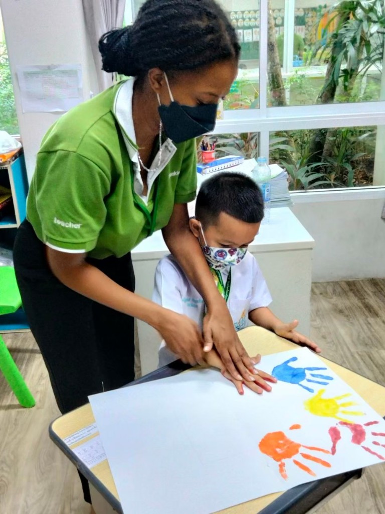 Teacher helping a student with a hand-painting activity in an Asian classroom